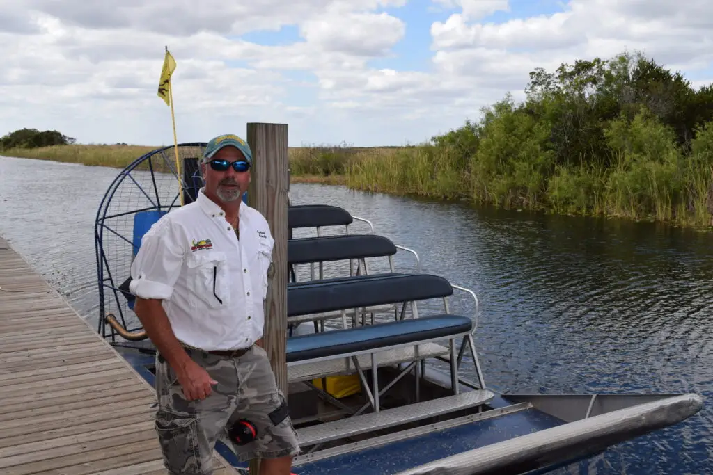 Captain Randy standing beside a private Everglades airboat docked along a canal in South Florida, preparing for a guided airboat tour.