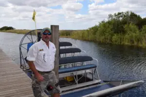 Captain Randy standing beside a private Everglades airboat docked along a canal in South Florida, preparing for a guided airboat tour.