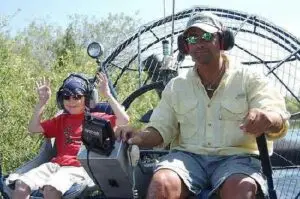 Young guest enjoying a private airboat adventure with Captain Randy while learning the controls during an interactive Everglades airboat experience with Ride The Wind.