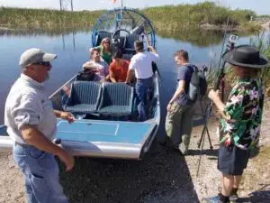 Private airboat charter loading passengers before an Everglades airboat tour with captain guiding guests aboard in shallow South Florida wetlands.